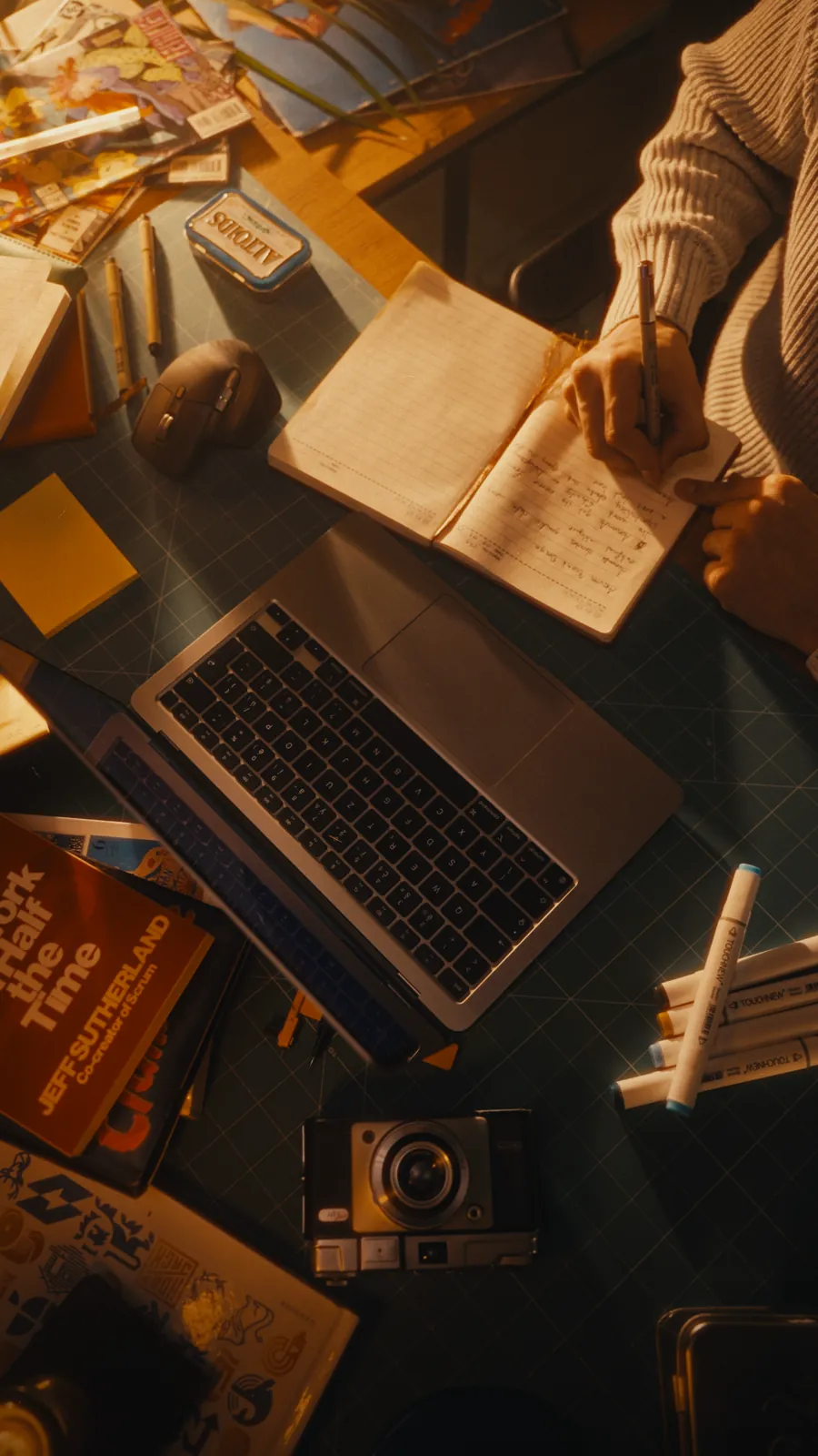 Hand writing in a notebook beside a laptop on the studio desk, from above