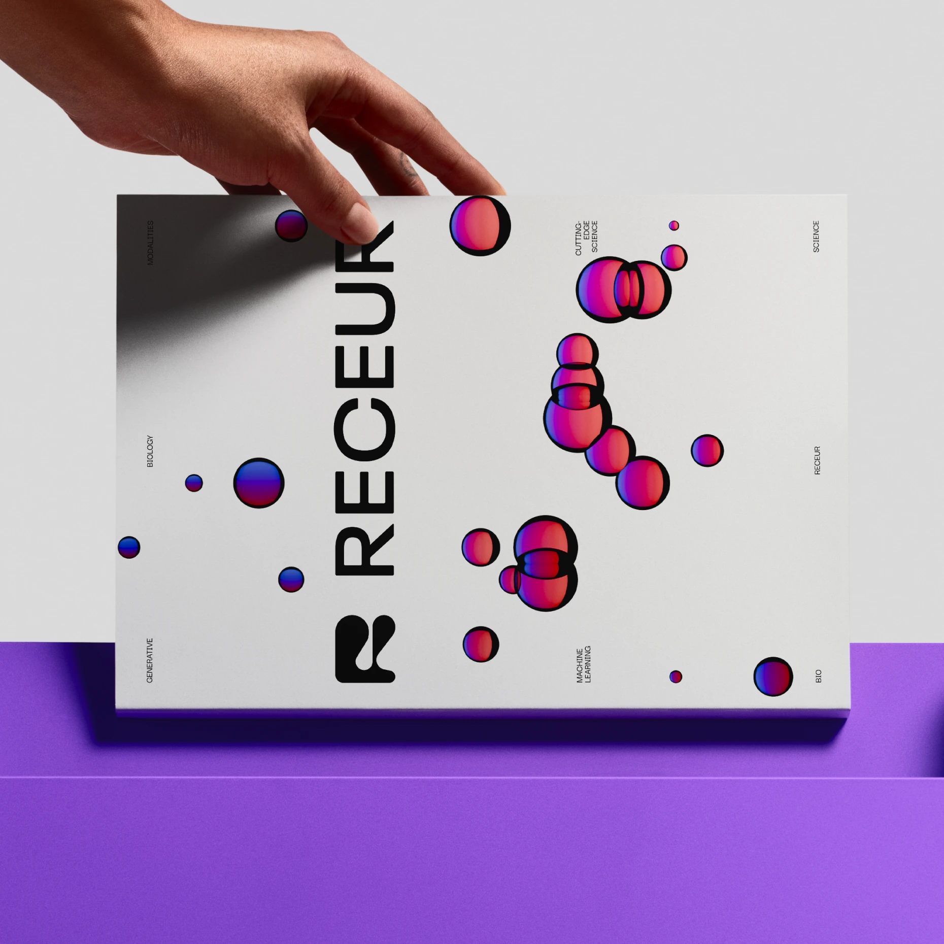 Hand holding a Receur brochure with the R mark, wordmark and floating cell spheres